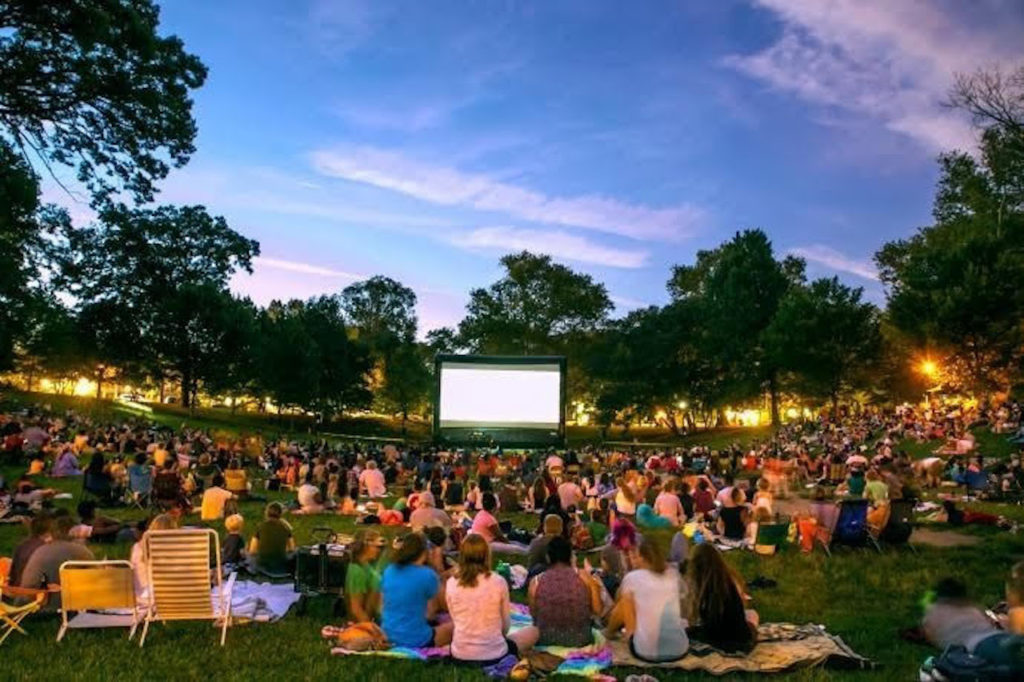people sitting on grass at dusk waiting for projector to play movie in the park