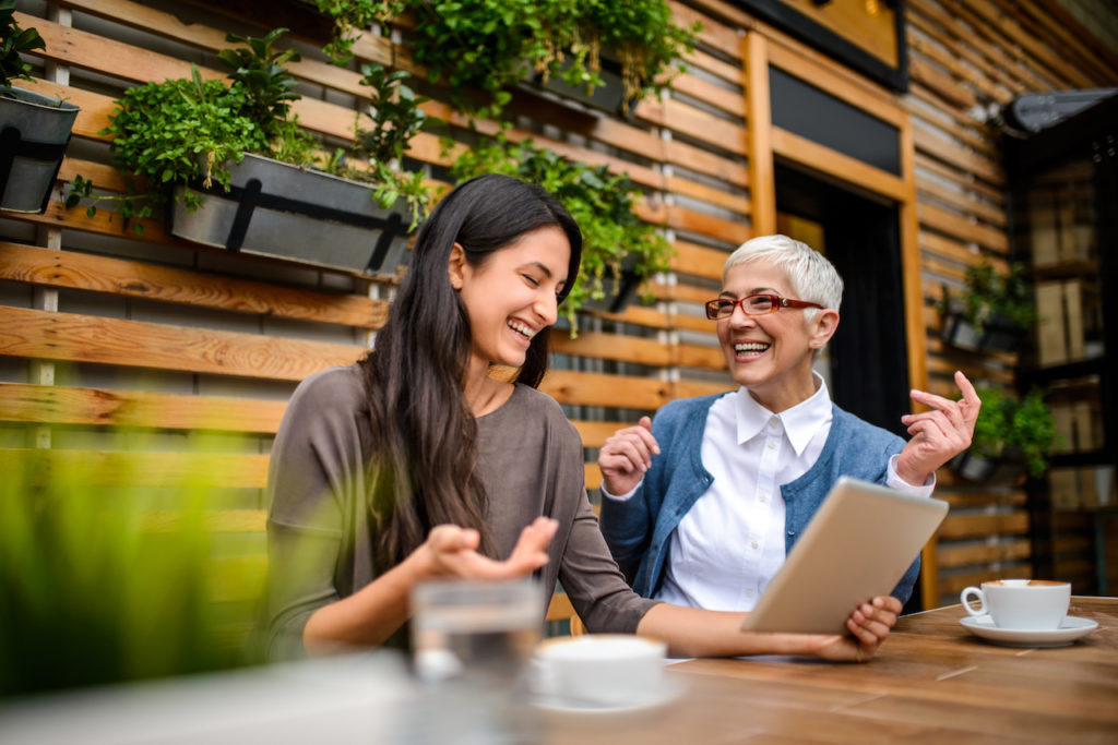 two women laughing while sitting at a table outside