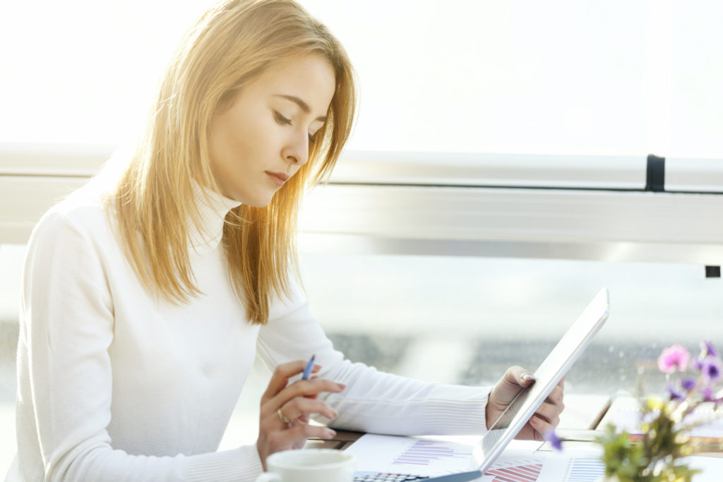 woman sits at a desk while looking at tablet