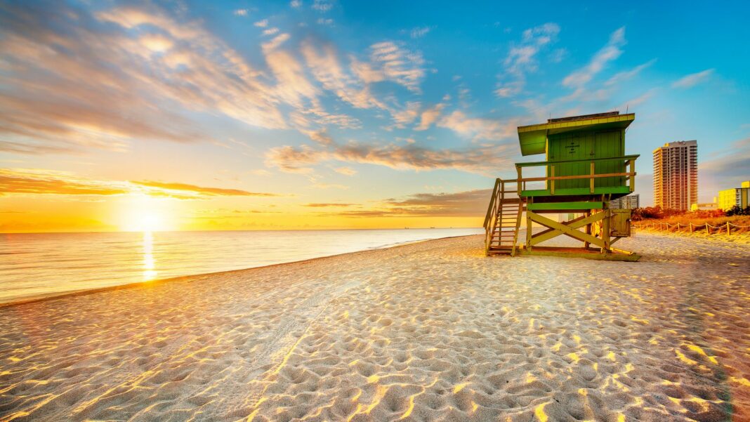 Miami South Beach sunrise with lifeguard tower and coastline with colorful cloud and blue sky.