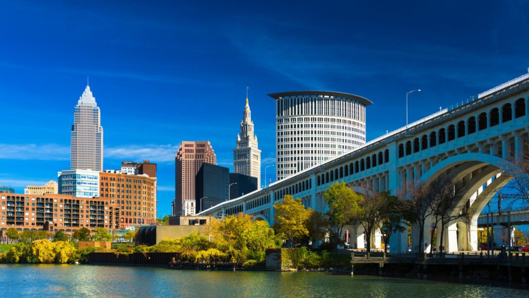 Downtown Cleveland skyline (featuring Key Tower) with the Cuyahoga River, Detroit-Superior Bridge, Autumn colored trees, and a deep blue sky with wispy clouds. Wide Angle.