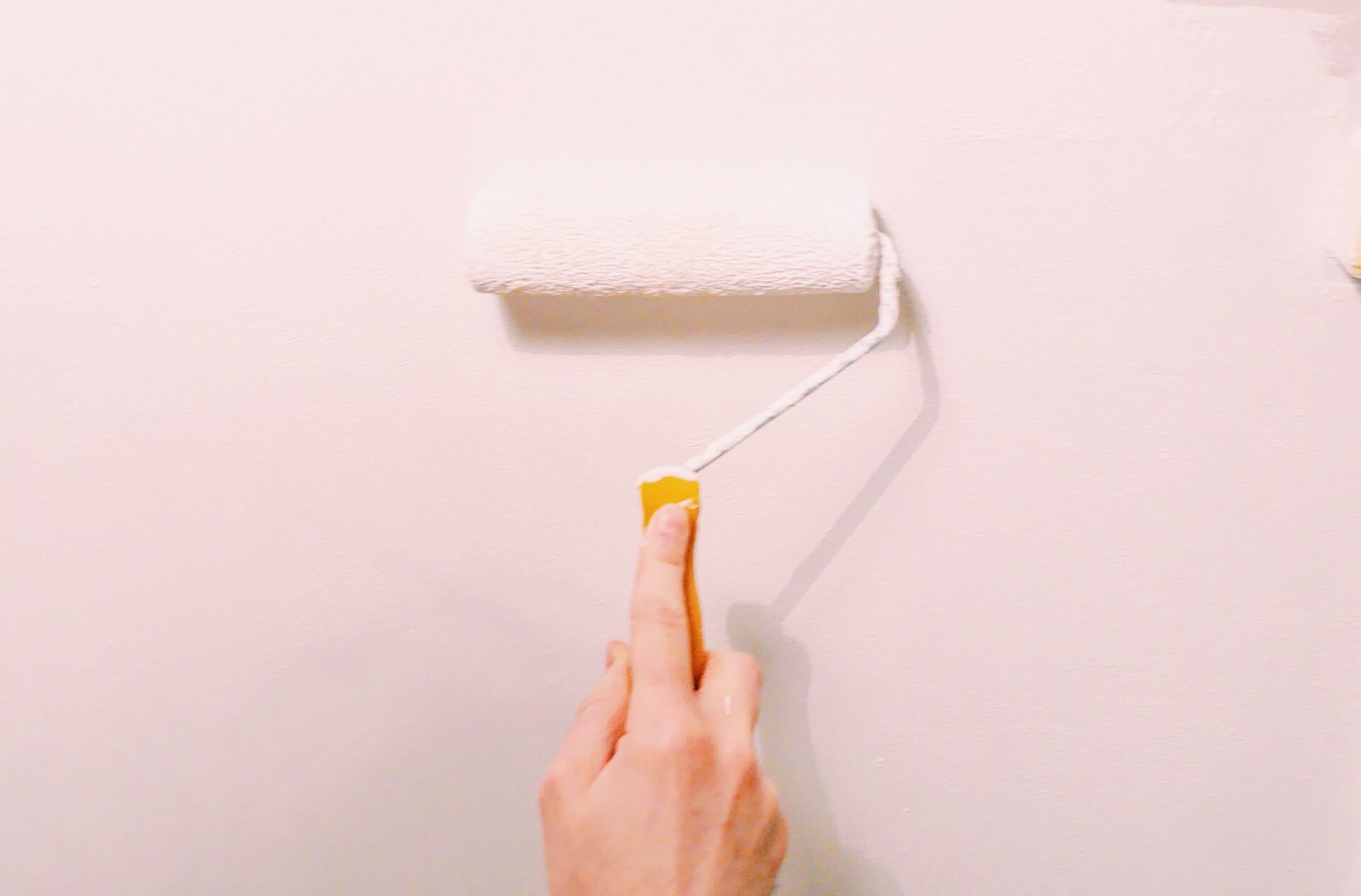 person's hand painting pink paint onto wall