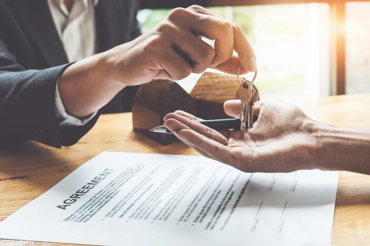 landlord handing over keys to apartment to renter with lease agreement on table