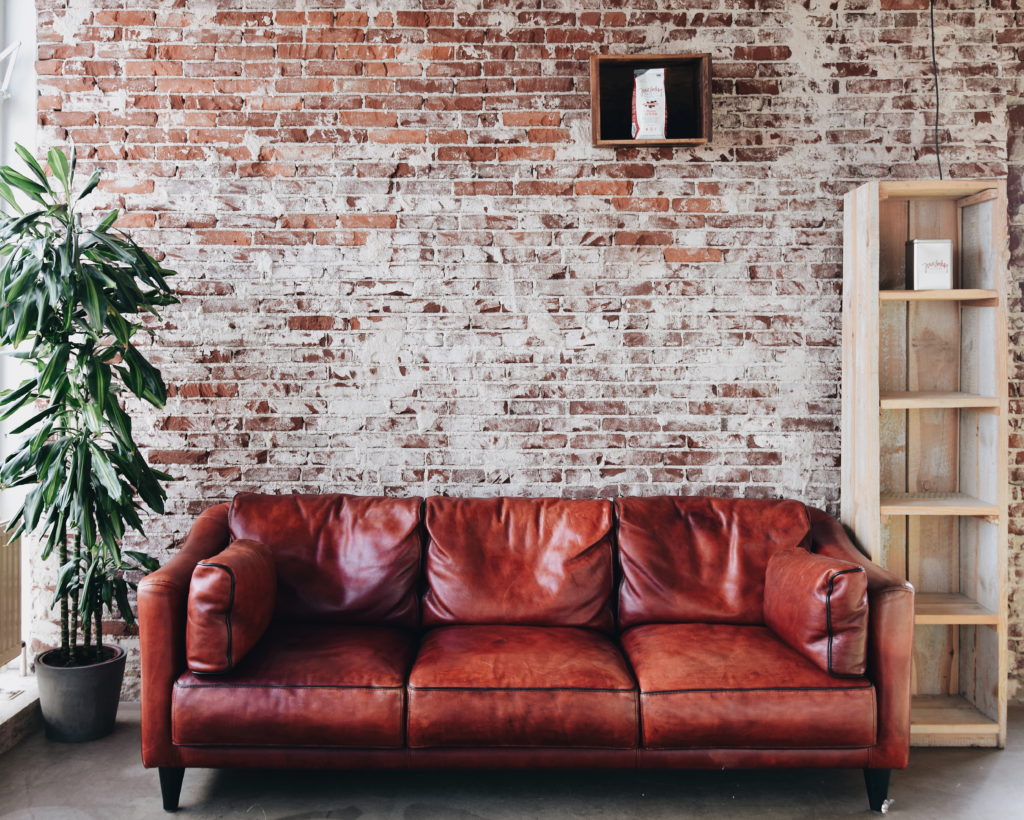 exposed brick wall with brown leather couch and plant